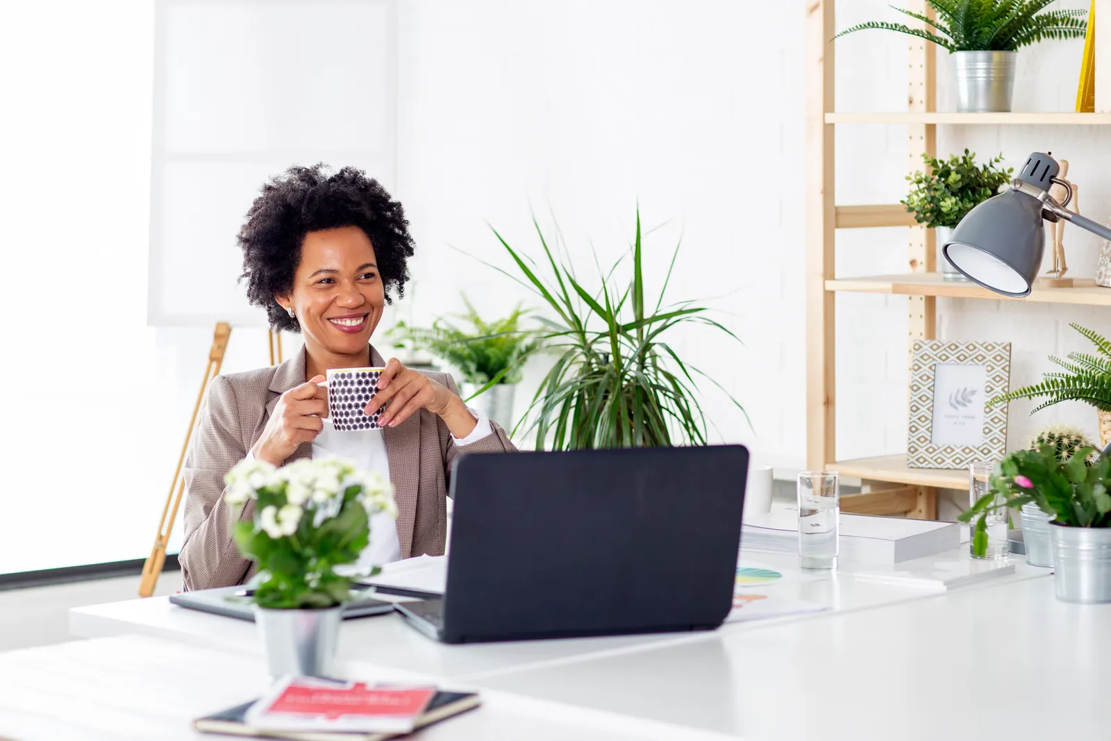 Businesswoman smiling with a coffee mug at her laptop in a bright office