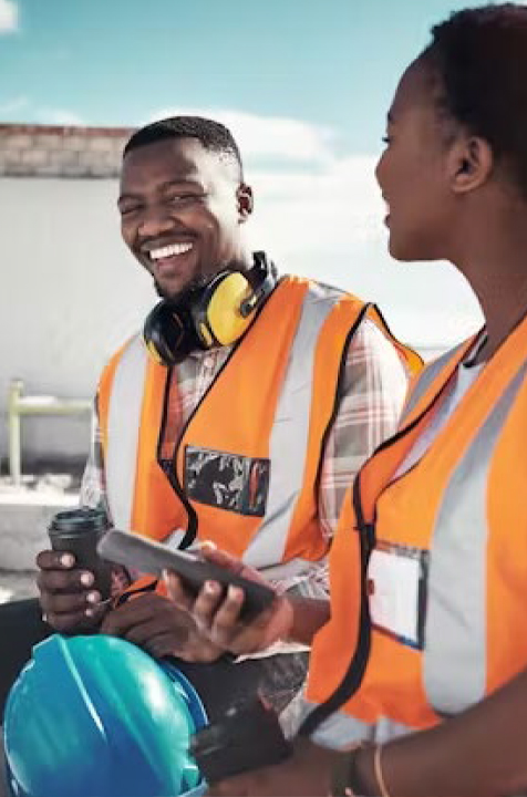 Two workers in high-visibility vests and hard hats smiling on site